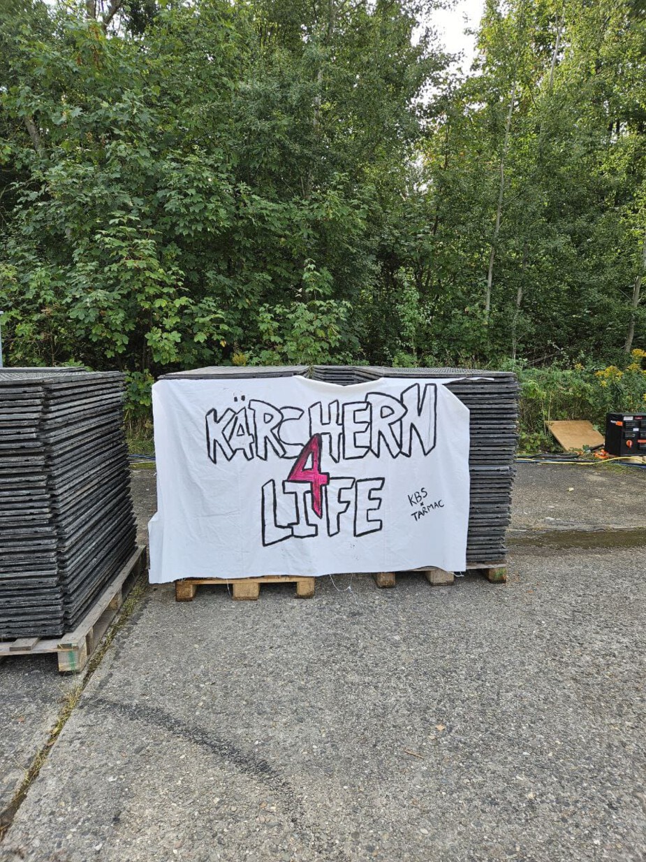 Several stacks of heavy-duty mats are lined up next to each other. A large banner hangs above the stack in the middle, bearing the inscription ‘KÄRCHERN 4 LIFE’.